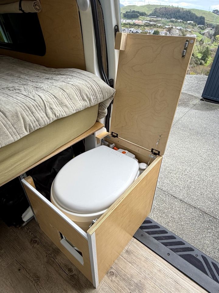 The cassette toilet in its plywood drawer, pulled out beside the bed