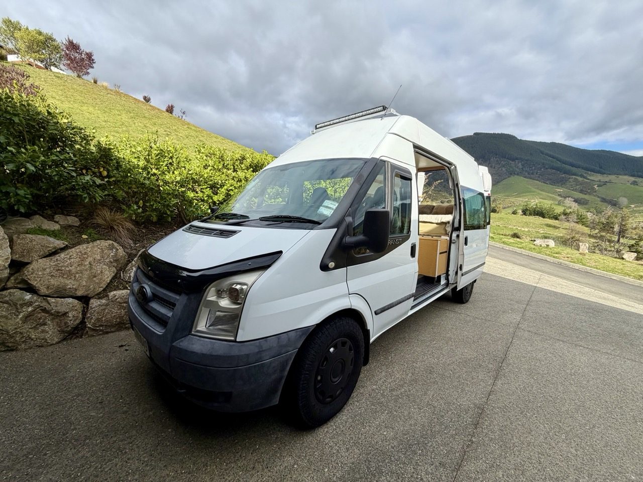 The camper parked on a driveway above green Nelson farmland with the sliding door open