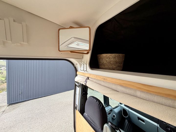 Storage shelf above the cab with a woven basket and a mirror on the wall
