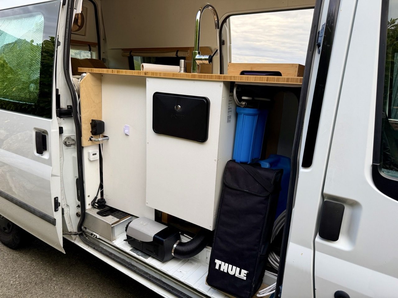Side door open showing the water filter housing, diesel heater and stored hoses under the bench