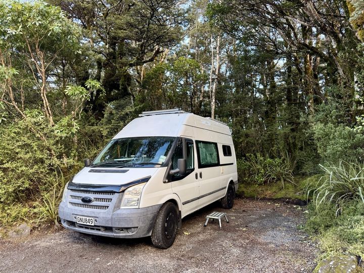 The camper parked on gravel surrounded by mossy beech forest